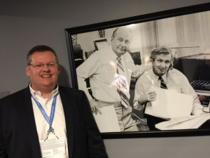 John Winborn, CIO for the Dallas Cowboys, poses next to a picture of two other innovators, Tex Schramm and Gil Brandt